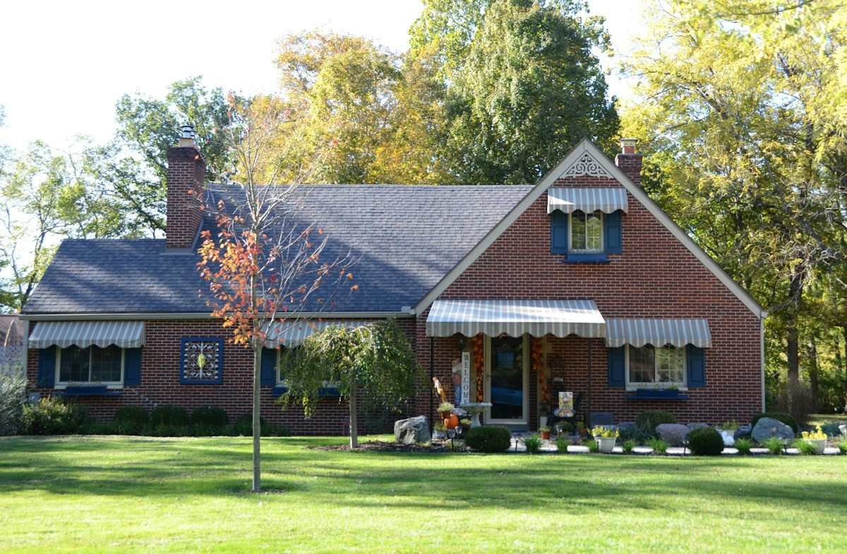 A red brick house with striped awnings among autumn trees