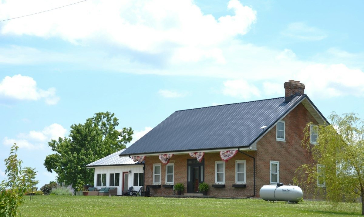 A brick farmhouse with a dark metal roof and a wide lawn