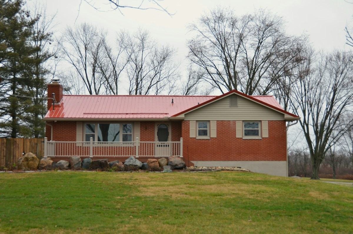 A brick ranch house with a red metal roof and a front porch rail
