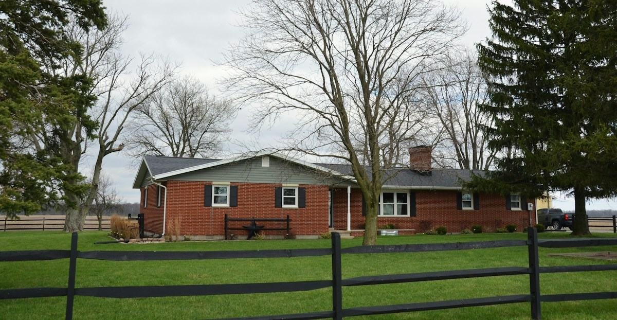 A long brick ranch house behind a split-rail fence and bare trees