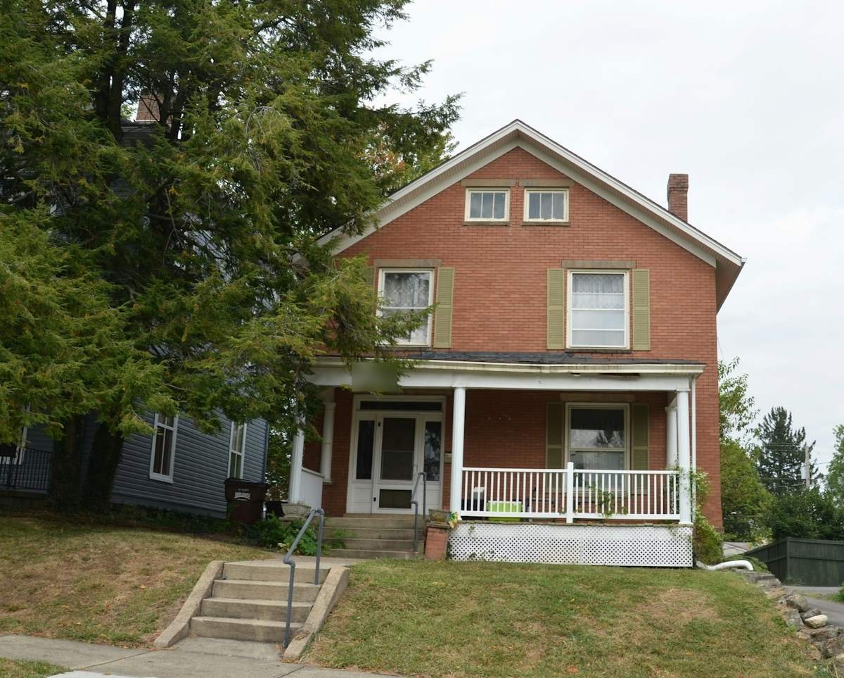 A two-story brick house with a front porch on a sloped yard