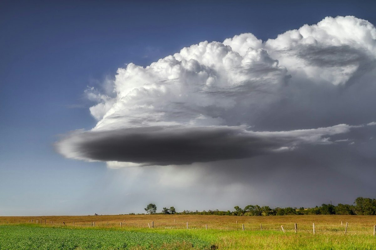 A towering storm cloud dropping rain over open fields